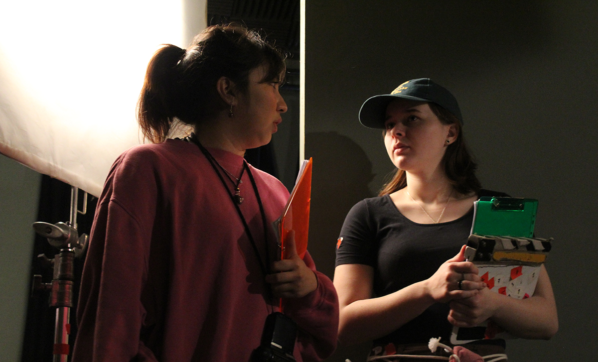 Two students talking, one holding a clapperboard